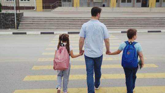 Parent leads children across pedestrian crossing